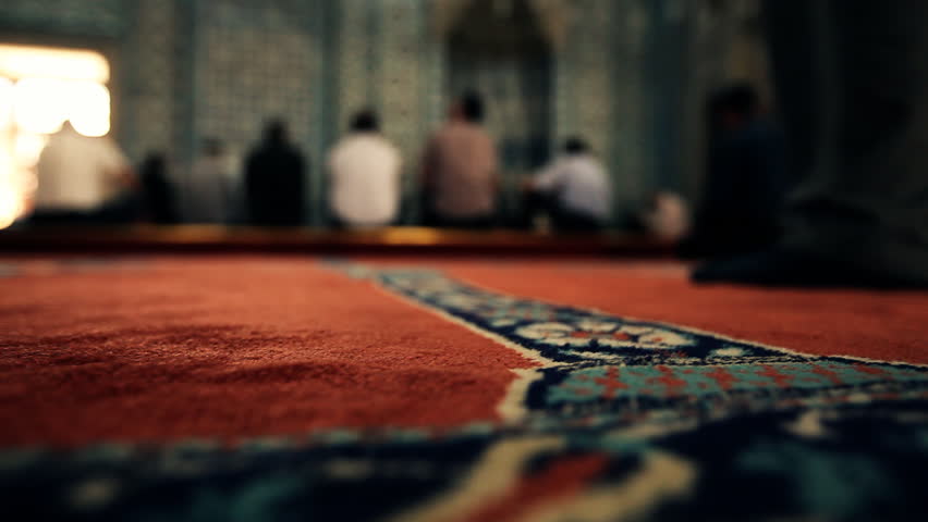 Close up of a carpet in a richly decorated mosque with unfocused people praying