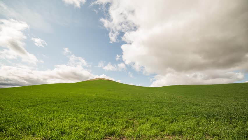 Time lapse of blue sky, green field on a cloudy afternoon