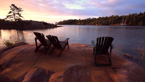 Scenic setting of Ontario cottage country, with three Muskoka Chairs aka Adirondack Chairs, at sunrise