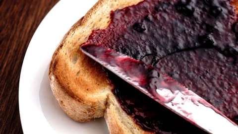 Spreading blueberry blackberry blackcurrant jam on crunchy toast in slow motion
