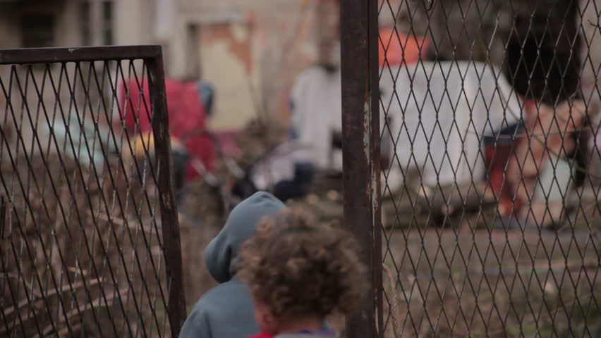 View through the lattice gate on gypsy ruined house. Poor gypsy family in the backyard. Male gypsy preparing firewood and two little kids come home after begging. Father blurred and children in focus. Royalty-Free Stock Footage #8844886