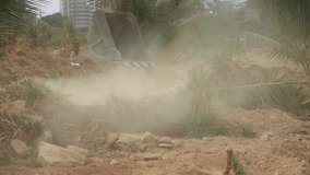 Stock Video Footage 1920x1080 Excavator on a construction site equates land clearing a building site, excavator bucket working as a hand on a background of a modern condominium building. Static, HDV
