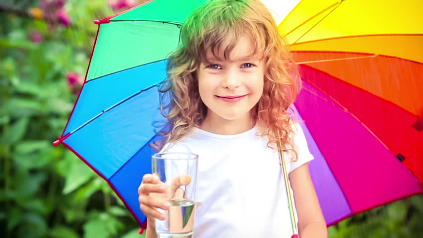 Happy child drinking water outdoors. Kid having fun in the rain. Slow motion