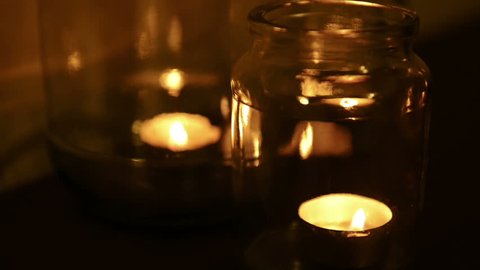 Small tea light candles burning in glass jars at night