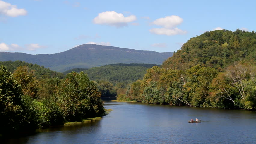 Two people fish from a small motorboat on the James River as seen from the Blue Ridge Parkway with the Blue Ridge Mountains which is located in the George Washington National Forest in Virginia.