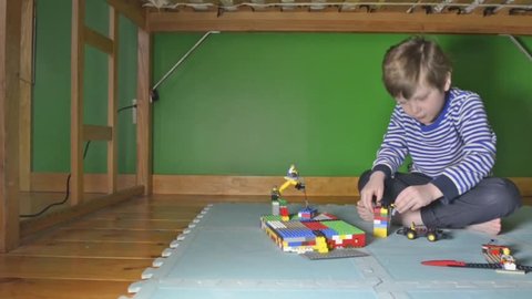 Tracking dolly shot of young boy playing with Lego on floor in his room