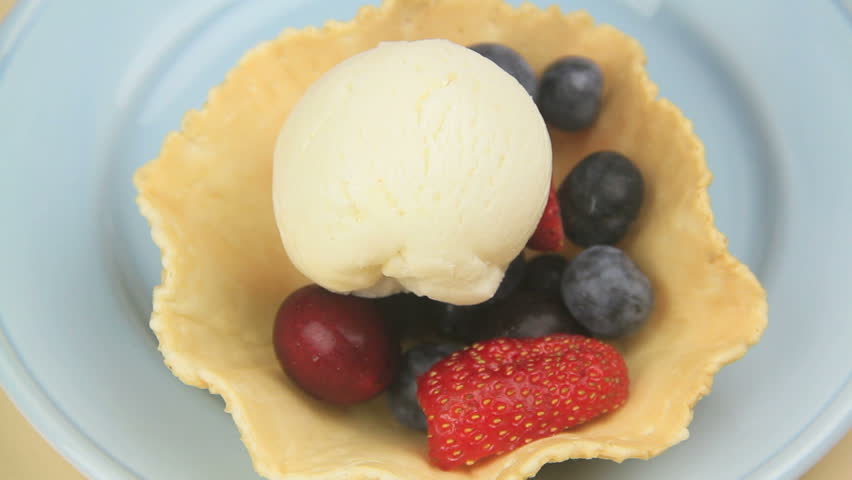 Chocolate sauce being poured over a scoop of ice cream in a crispy basket  of berries to prepare a berry dessert.
