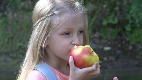 4K Little Girl Eating Apple Fruit by Brook, Portrait, Face of Kid Taking a Snack in Nature, Blonde Child Relaxing after Hiking in Mountains Trail, Children in Camping, Summer Vacation, Healthy Food