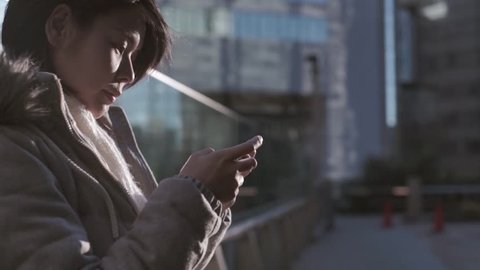 Slow-motion shot of young Japanese girl using smartphone in office district in Tokyo Stock Video