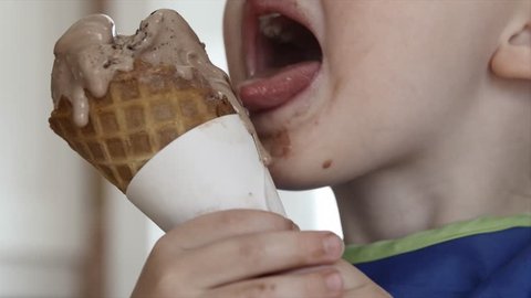 A mother givers her toddler boy an ice cream cone to eat in the kitchen