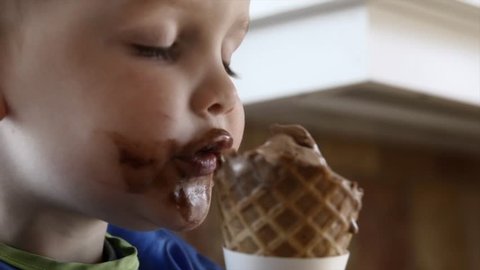 A mother givers her toddler boy an ice cream cone to eat in the kitchen