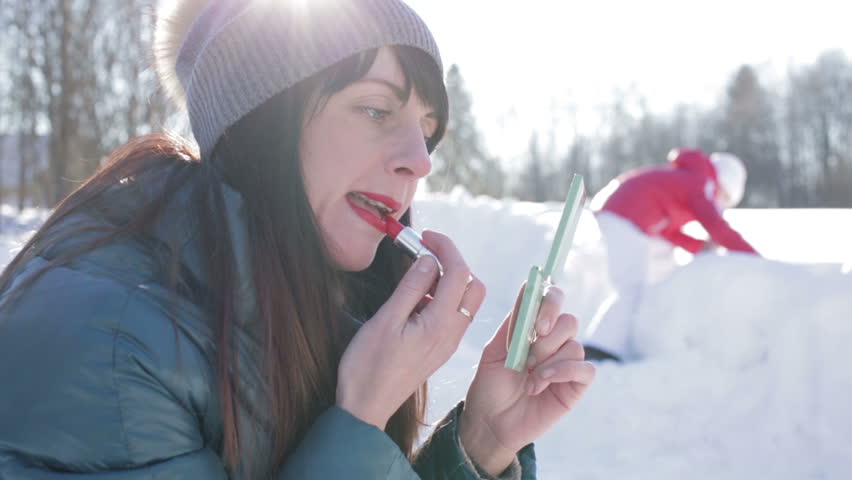 Girl applies lipstick winter outdoors