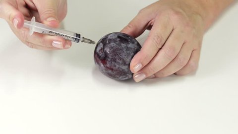 Poisoned plum. Someone's hands are making poison injection into plum with syringe