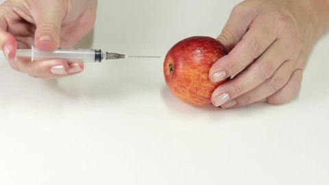 Poisoned apple. Someone's hands are making poison injection into apple with syringe