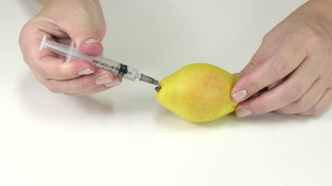 Poisoned pear. Someone's hands are making poison injection into pear with syringe