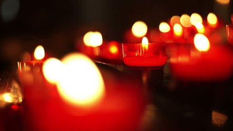 Red votive candles close up.
Small, votive candles flickering in red holders. Mostly blurred but one of them is 
in focus.