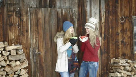 Young women standing outside chalet and enjoying coffee during winter