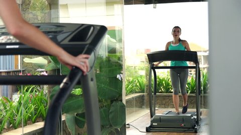 Young woman running on treadmill in gym in front of the mirror
