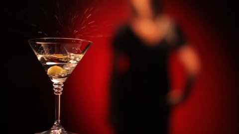 Olive falls in a glass of martini. Female silhouette on a red background