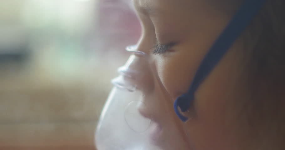 Girl sitting in bed in the hospital and inhales. The girl is sick, coughing, sad, not funny, treatment in the hospital, at the doctor's. Inhalation mask on her face. Royalty-Free Stock Footage #8911858