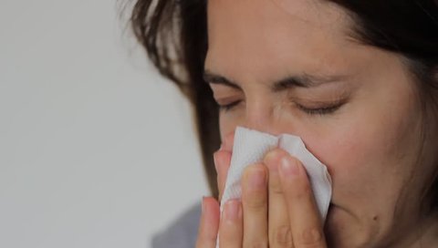 Woman with a flu is blowing her nose using a napkin.