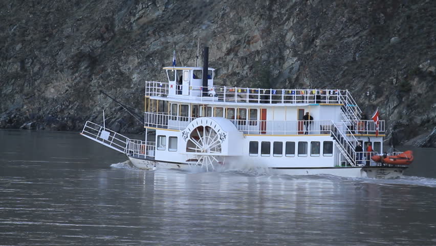 Boat with steam side paddles on Yukon River, Klondike gold area by Dawson City, Canada. Steaming upstream against current. Powerful ship for tourists, passengers and cargo.