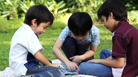 Three little boys playing a board game sitting in park
