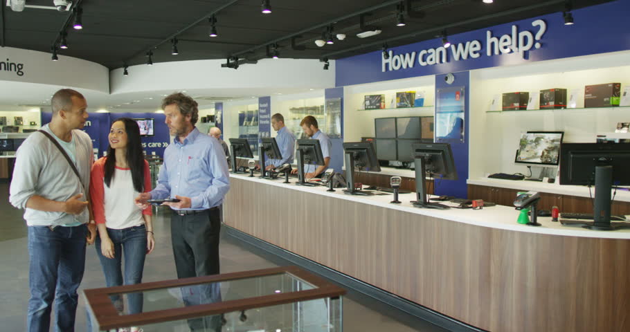4K Helpful salesman serving customers in consumer electronics store showroom