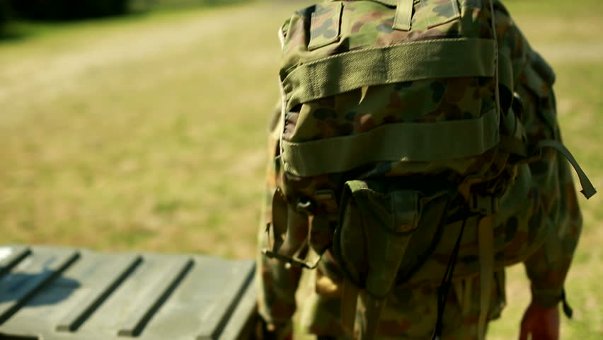 Military army officers wearing camouflaged uniforms and army boots, carrying military backpacks, trunks, and supplies march in an field to their army base Royalty-Free Stock Footage #8946802