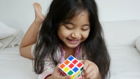 PHITSANULOK, THAILAND - FEBRUARY 10 : Little Asian girl playing with rubik's cube on the bed on February 10, 2015 in Phitsanulok, Thailand