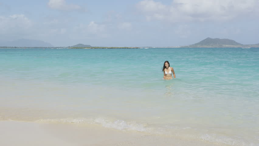Woman at beach walking out of sea in bikini after swimming in the ocean on vacation travel getaway holidays. Beautiful young multiracial Asian Caucasian female model, 20s. Lanikai, Oahu, Hawaii, USA.