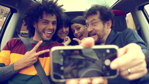 Four cool people in car taking selfie with smartphone smiling happy : vidéo de stock