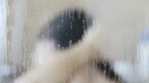 A woman washing her hair behind a glass wall in a shower