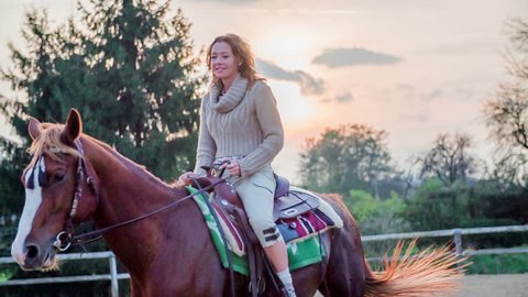 Woman on the horse with a sunset in the background. Slow motion RAW footage of a beautiful woman riding the horse on a ranch with beautiful sunset in the background.