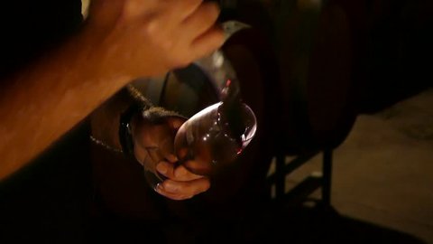 Close up of wine glass being filled to test red wine in winery cellar featuring rows of oak barrels after vintage and harvest. Include Barossa Valley, Clare valley, Hunter Valley, Tanunda, Yarra,
