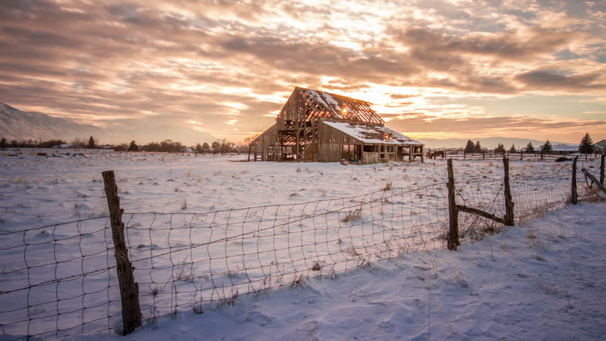 Time-lapse video at sunset with a barn in a snow filled field.
