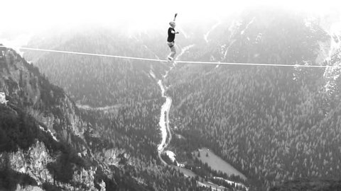 aerial shot of tightrope walker in the air in the mountain with snow black and white