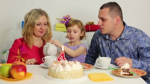 Little girl pours out tea to her parents sitting at birthday table.
