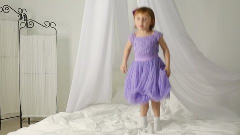 Little girl in dress is jumping on the bed with white baldachin.
