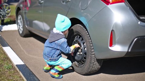 Little girl and boy tie rear wheel of car with socket wrench.

