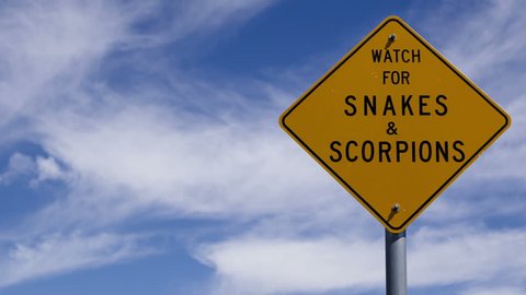 4K Time lapse close up of watch for snakes and scorpions sign with partly cloudy blue sky background