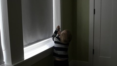 A toddler opens the blinds in his window to let more light into his bedroom