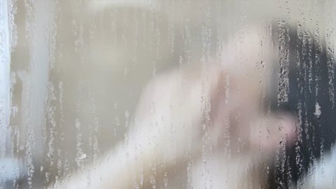 A woman washes her hair in a hot shower behind a glass wall