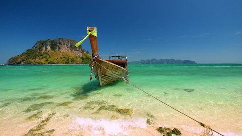 Thai traditional wooden boat with ribbon decoration at ocean shore under blue sky.Thailand tropical beach landscape, Krabi province