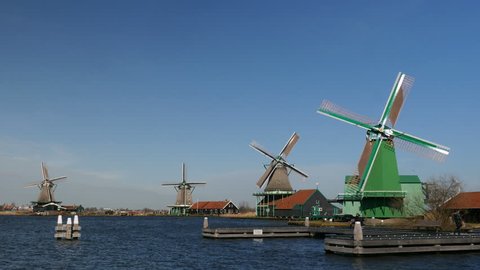 Four picture perfect Dutch windmills on the waterfront with blades turning at the Zaanse Schans in Holland. Perfectly blue sky.
