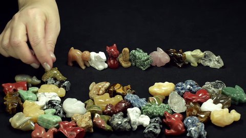 Woman hand is choosing 12 Chinese zodiac stone animals from assorted gemstone figurines on black background
