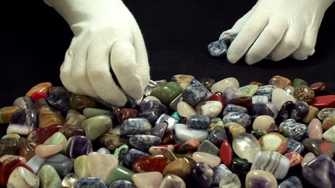 Womans hands are making sodalite stone line from assorted gemstones on black background.