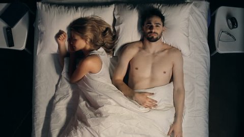 Direct from above view of couple in bed, woman sleeping, man tossing sleeplessly