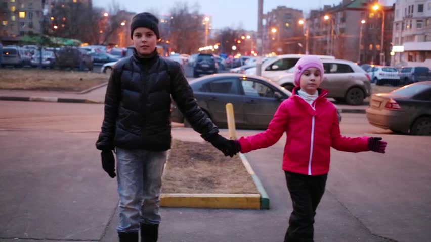 Boy and girl hold hands and walk on border on street at spring day