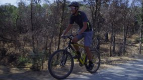 Man riding mountain bike down gravel road, tracking shot